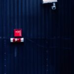 Modern security camera and exit sign on a corrugated metal wall, emphasizing surveillance and safety.